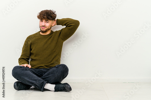 Young Moroccan man sitting on the floor isolated on white background suffering neck pain due to sedentary lifestyle. © Asier
