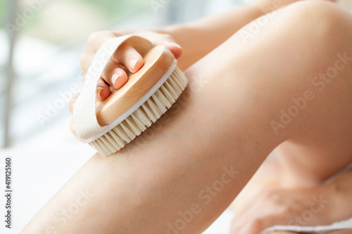 Cellulite treatment, woman arm holding dry brush to of her leg. photo