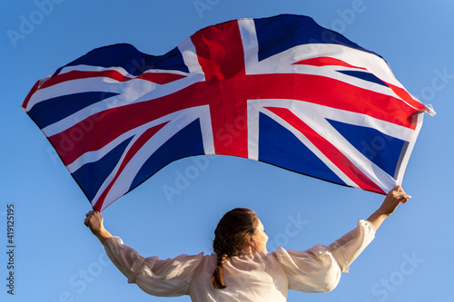 The flag of England waving in the hands of a woman against the blue sky. View from the back. Great Britain, victory and success photo