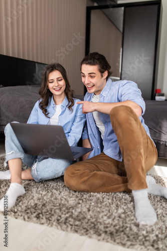 Young couple sitting on the floor in the bedroom and looking at a tablet screen and a laptop in the morning.