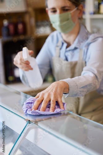Female Owner Delicatessen Wearing Face Mask Cleaning Counter With Sanitising Spray