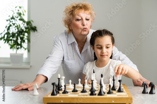 Young girl playing chess with grandmother together at home