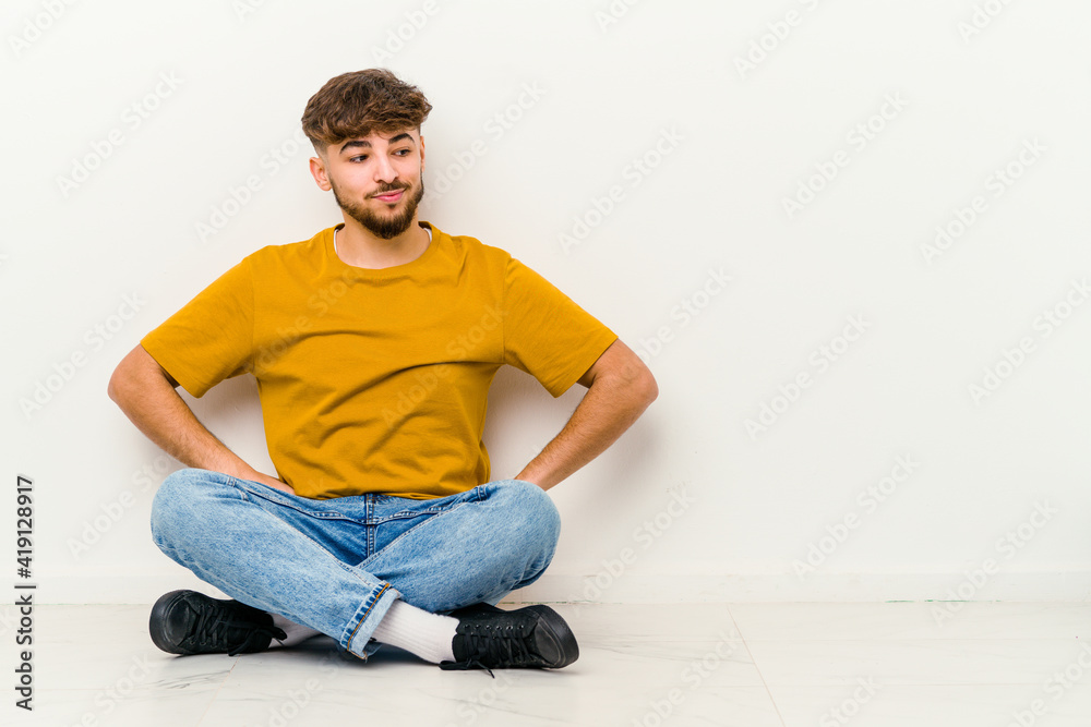 Young Moroccan man sitting on the floor isolated on white background dreaming of achieving goals and purposes Young Moroccan man sitting on the floor isolated on white background dreaming of achieving goals and purposes