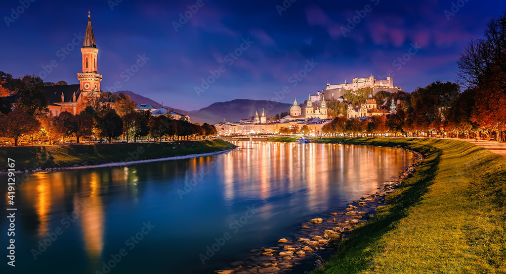 Obraz premium Beautiful view of Festung Hohensalzburg and Castle Hohensalzburg during sunset with colorful sky with reflection in Salzach river in evening, Salzburg, Austria. Popular travel and historical center