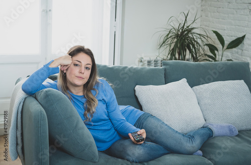 Bored woman watching TV at home changing channels with remote control