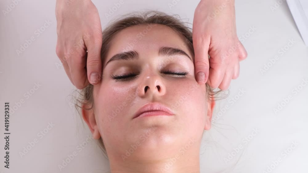 Facial massage beauty treatment. Close up of a young womans face lying on back, getting face lifting massage, pinch and roll technique Facial massage beauty treatment. Close up of a young womans face lying on back, getting face lifting massage, pinch and roll technique