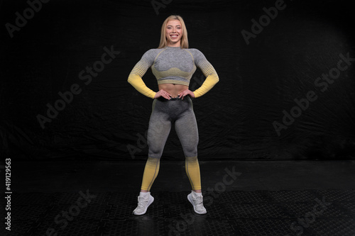 athletic girl of European appearance in fitness clothes posing against a dark background, emphasizing her muscles