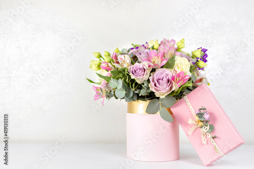 Foto Beautiful bouquet of flowers in round box and pink gift box on a white table