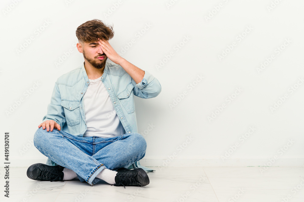 Young Moroccan man sitting on the floor isolated on white background having a head ache, touching front of the face.