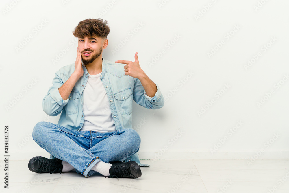 Young Moroccan man sitting on the floor isolated on white background having a strong teeth pain, molar ache.