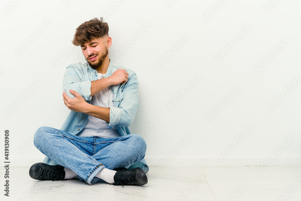 Young Moroccan man sitting on the floor isolated on white background massaging elbow, suffering after a bad movement. Young Moroccan man sitting on the floor isolated on white background massaging elbow, suffering after a bad movement.