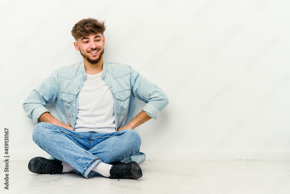 Young Moroccan man sitting on the floor isolated on white background laughs and closes eyes, feels relaxed and happy. Young Moroccan man sitting on the floor isolated on white background laughs and closes eyes, feels relaxed and happy.