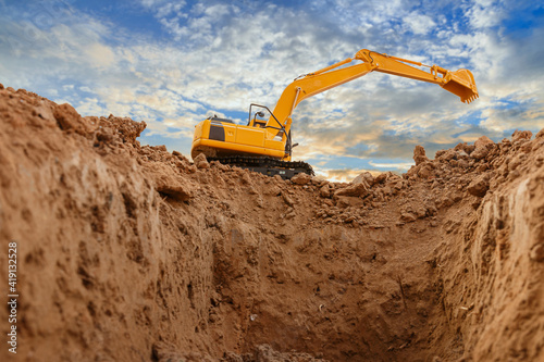 Yellow excavators are digging the soil in the construction site on the sky and cloud background,With bucket lift up.