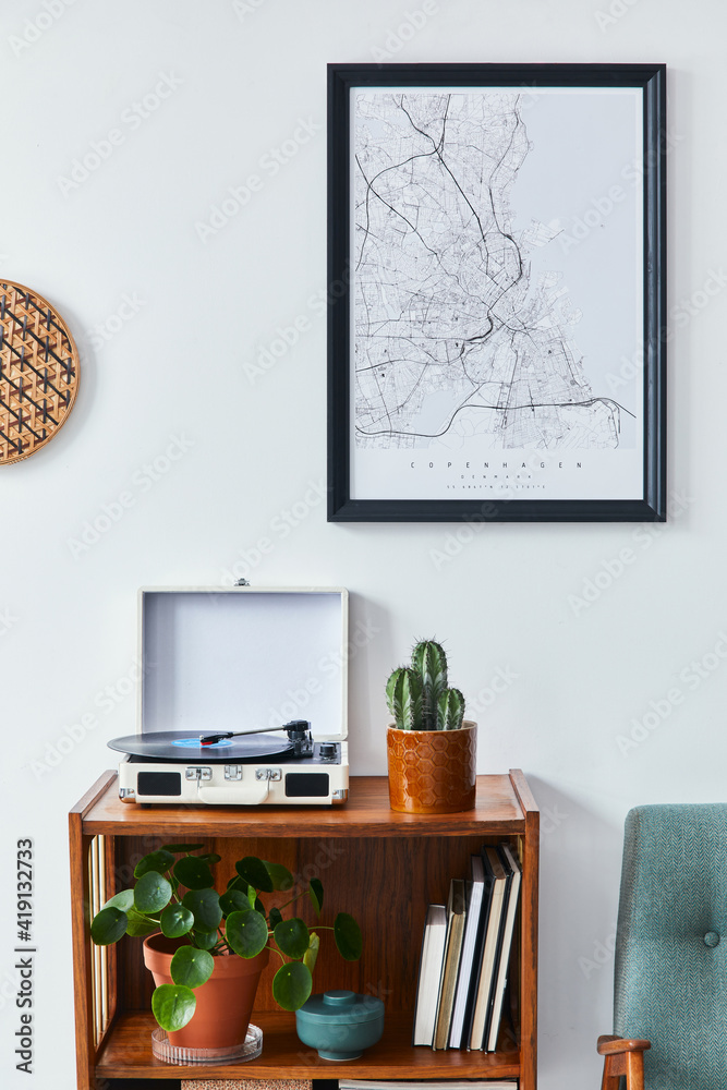 Fototapeta premium Retro composition of living room interior with mock up poster map, wooden shelf, book, armchair, plant, cacti, vinyl recorder and personal accessories in stylish home decor.