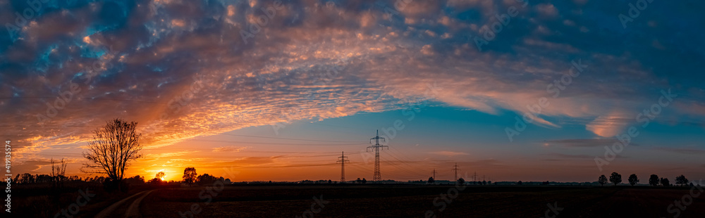 High resolution stitched panorama of a beautiful sunset with a dramatic sky and overland high voltage lines near Tabertshausen, Bavaria, Germany