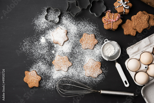Star shaped baked gingerbread cookies sprinkled with powdered sugar on a black table