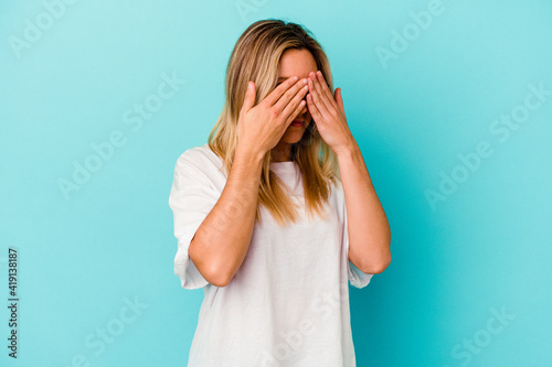 Young mixed race woman isolated on blue background afraid covering eyes with hands. © Asier