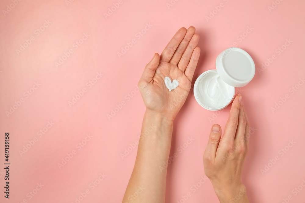 Revitalizing hand cream for healing and recovery after excessive use of soap and disinfectants. Young woman applying moisturizing lotion. Copy space, close up, pink background, flat lay, top view. Revitalizing hand cream for healing and recovery after excessive use of soap and disinfectants. Young woman applying moisturizing lotion. Copy space, close up, pink background, flat lay, top view.