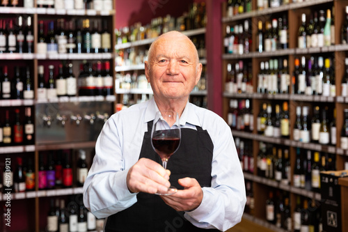 Successful elderly male owner of winery inviting to tasting wine of own production. High quality photo