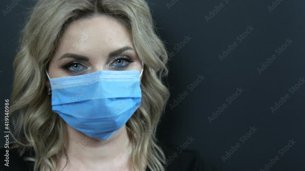 A beautiful young woman with evening make-up smoky eyes and a black dress in a medical protective mask on a black background looks into the camera. Covid, pandemic, quarantine. Copy space. A beautiful young woman with evening make-up smoky eyes and a black dress in a medical protective mask on a black background looks into the camera. Covid, pandemic, quarantine. Copy space.