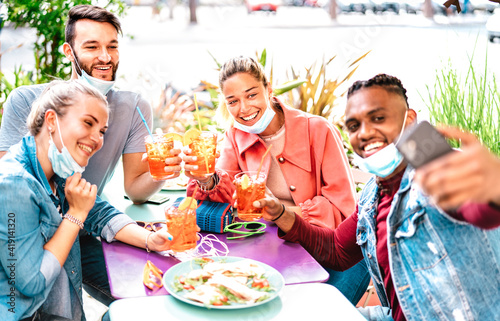 Multicultural people taking selfie with open face masks at cocktail bar - New normal life style concept with young friends having fun toasting together at restaurant garden party - Bright warm filter