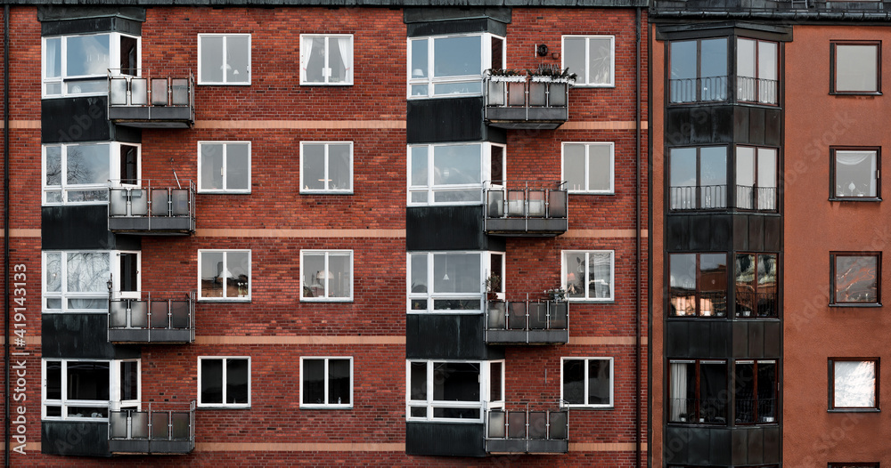 Housing development in Scandinavian style. In middle, building is dominated by brick facade, white window frames and tin balconies. Individual housing units have various decorations behind windows.