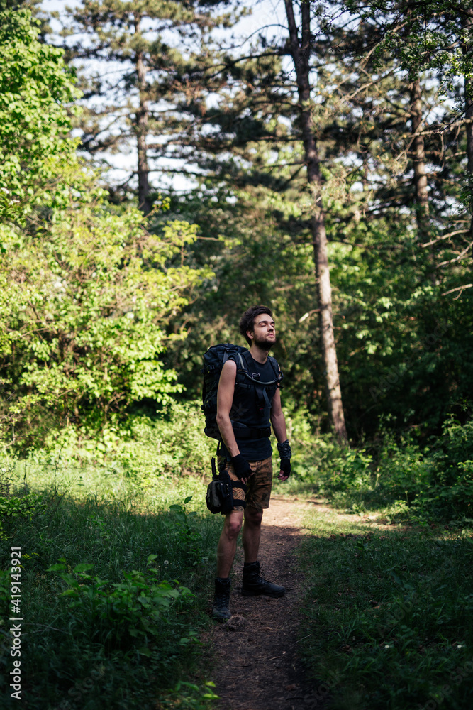 Man standing in forest and soaking up atmosphere. Man is dressed in shorts,undershirt and high boots.He carries large backpack with hydration bag on his back and thigh panel with equipment on his leg. Man standing in forest and soaking up atmosphere. Man is dressed in shorts,undershirt and high boots.He carries large backpack with hydration bag on his back and thigh panel with equipment on his leg.