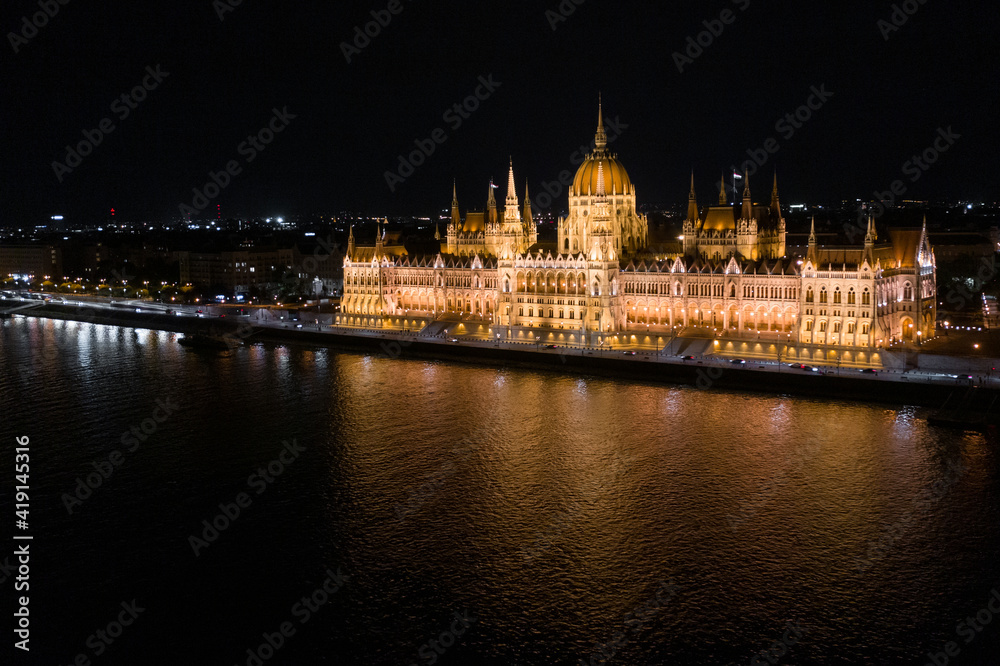 Aerial view of illuminated Budapest Parliament building at night with dark sky and reflection in Danube river. Panoramic view of hungarian Parliament building. Budapest, Hungary at night.