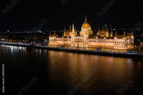 Aerial view of illuminated Budapest Parliament building at night with dark sky and reflection in Danube river. Panoramic view of hungarian Parliament building. Budapest, Hungary at night.