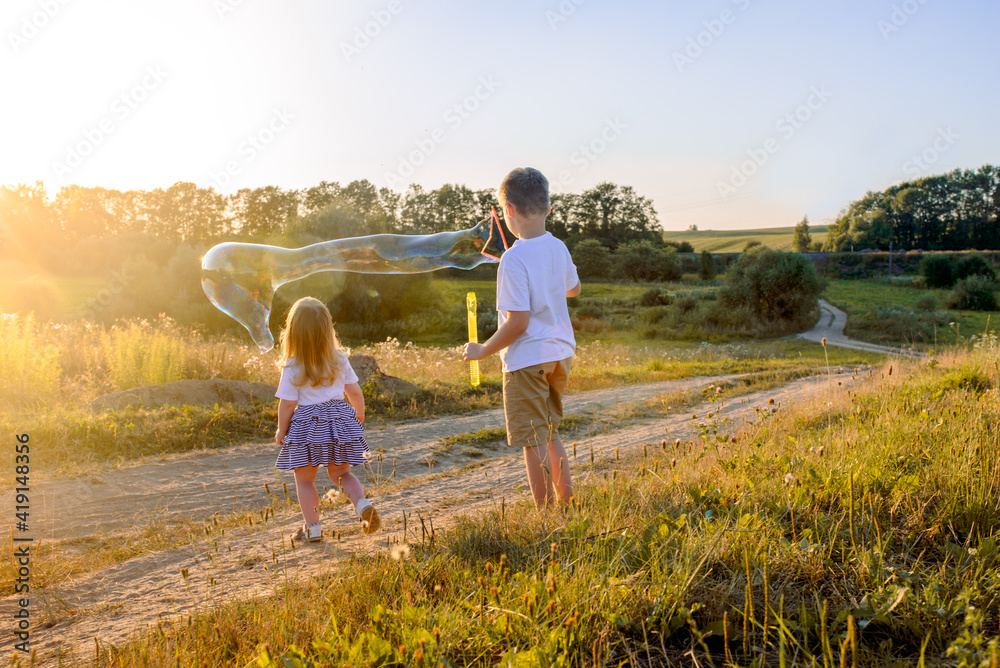 Fototapeta premium Happy children playing with soap bubbles on a summer nature. Bubbles in the sunset