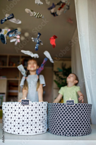 Household chores for children. Kids cleaning their room, sorting dry socks and arranging them into personal baskets with fun, they turn cleaning into the game. Everyday routine, lifestyle