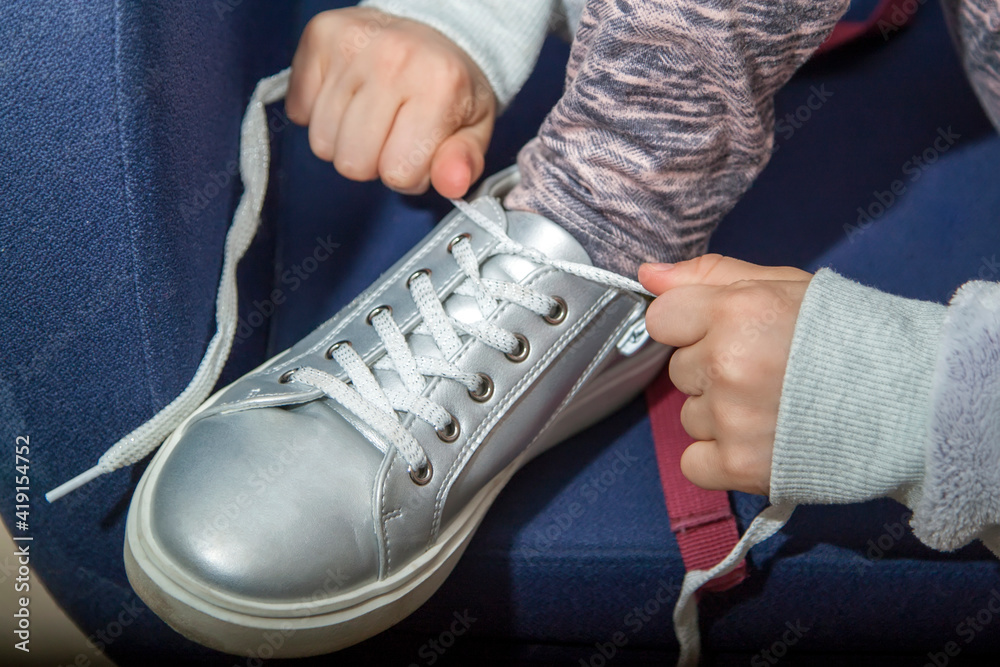 Close up kid girl hands tying shoelace on shoes before walk sitting on blue chair