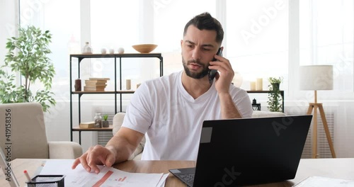 Man talking on the phone while working with a laptop at home on quarantine