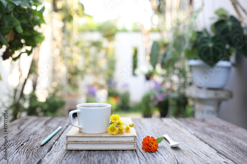 Fototapeta Naklejka Na Ścianę i Meble -  White coffee cup and flowers with pencil and notebooks on brown wooden table with garden view
