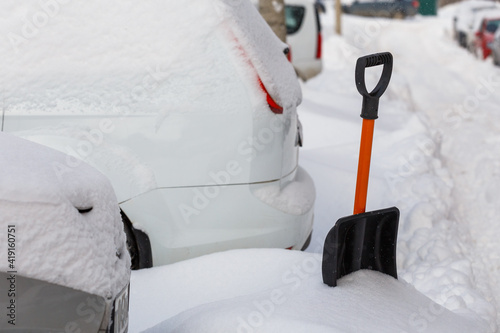 small plastic snow shovel near snow-covered cars at sunny winter morning photo