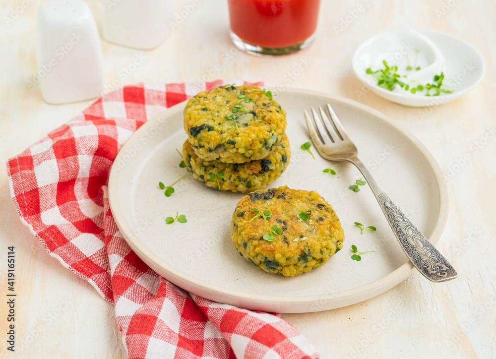 Fried burgers or cutlets of bulgur, carrots and spinach on a light ceramic plate on a light concrete background. Bulgur recipes. Fried burgers or cutlets of bulgur, carrots and spinach on a light ceramic plate on a light concrete background. Bulgur recipes.