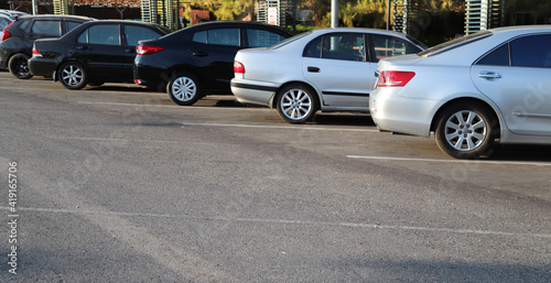 Closeup of rear, back side of blue car with other cars parking in outdoor parking area in bright sunny day. 