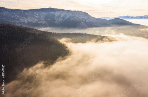Landscape scenery in morning mist illuminated by sunlight. Forest hills in sunny haze in sunrise with copy space. Mountains in orange fog form top view.
