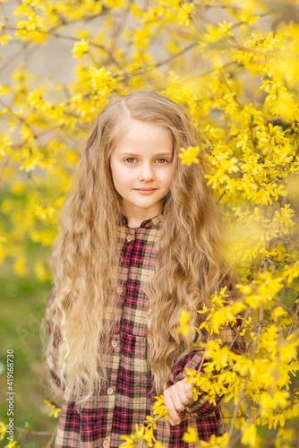 girl with long hair in yellow flowers. A child on the background of forsythia. Spring portrait of a child