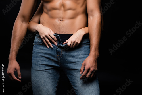 Cropped view of woman taking off jeans from sexy man isolated on black