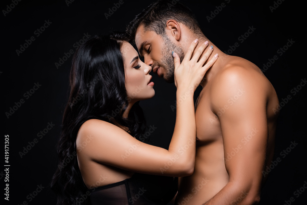 Side view of woman kissing shirtless boyfriend isolated on black Side view of woman kissing shirtless boyfriend isolated on black