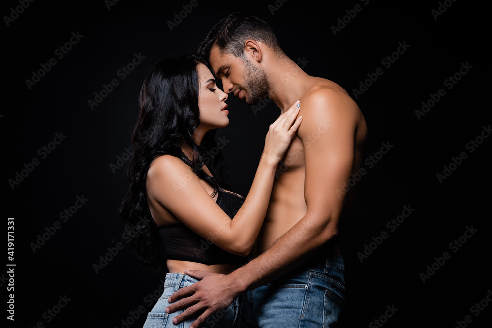 Side view of sexy couple in jeans standing with closed eyes isolated on black Side view of sexy couple in jeans standing with closed eyes isolated on black