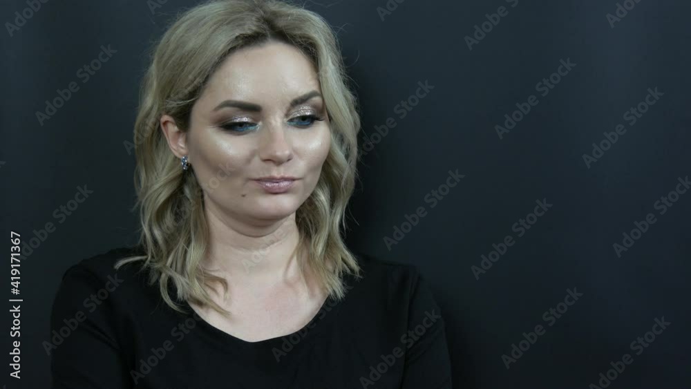 A beautiful young woman with bright evening make-up smoky eyes and a black dress looks thoughtfully on a black background. Girl model in studio. A beautiful young woman with bright evening make-up smoky eyes and a black dress looks thoughtfully on a black background. Girl model in studio.