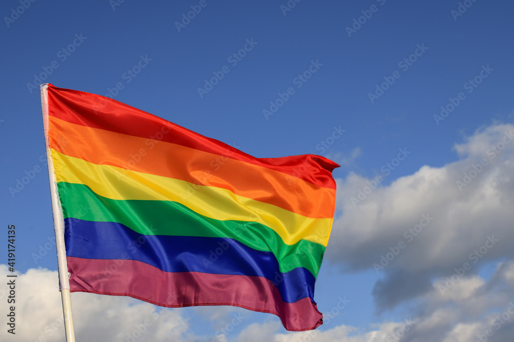 Waving gay pride rainbow flag in blue summer sky, copy space. Realistic flag of LGBT organization include lesbians, gays, bisexuals and transgender. Waving gay pride rainbow flag in blue summer sky, copy space. Realistic flag of LGBT organization include lesbians, gays, bisexuals and transgender.