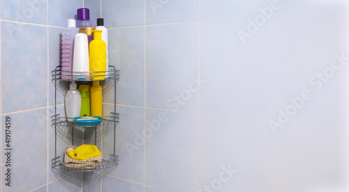 A metal bathroom grate shelf filled with body and hair care products weighs on a blue tile in the corner.
