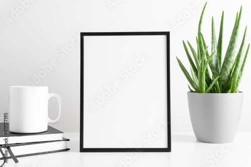 Black frame mockup with workspace accessories  mug of tea and aloe vera in pot on white table. Front view. Place for text  copy space  mockup