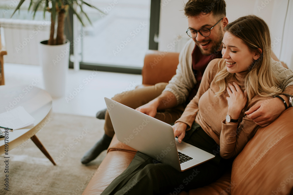 Young couple using laptop together while sitting on sofa at home Young couple using laptop together while sitting on sofa at home