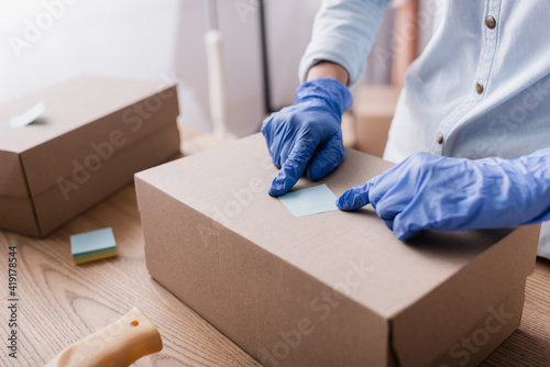 partial view of showroom owner in latex gloves fixing sticky note on carton box