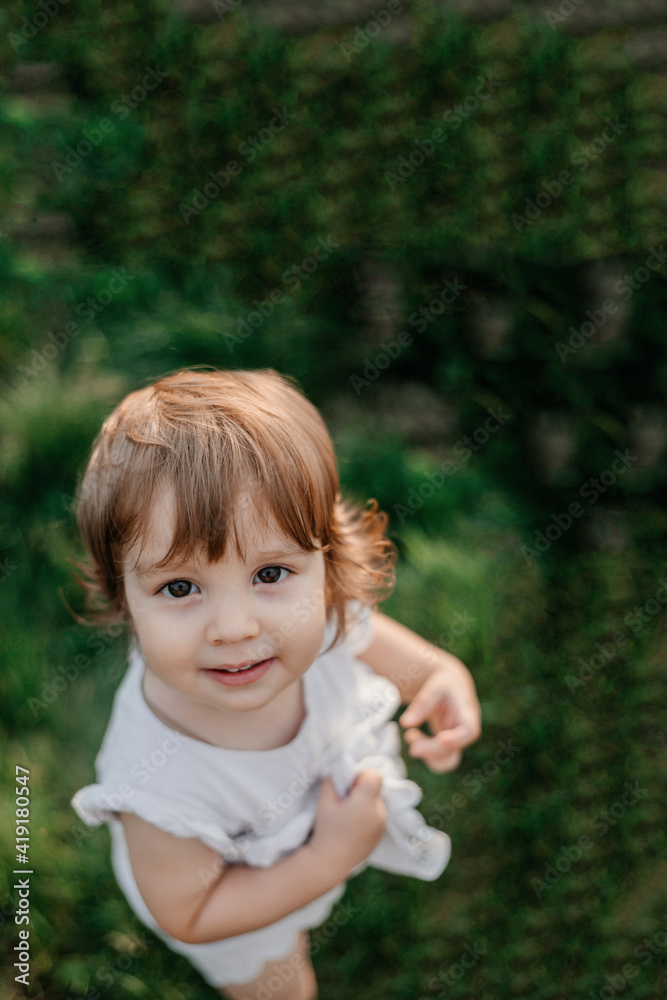 Portrait of a little girl in white clothes standing on the grass in summer. Fun and happy childhood Portrait of a little girl in white clothes standing on the grass in summer. Fun and happy childhood