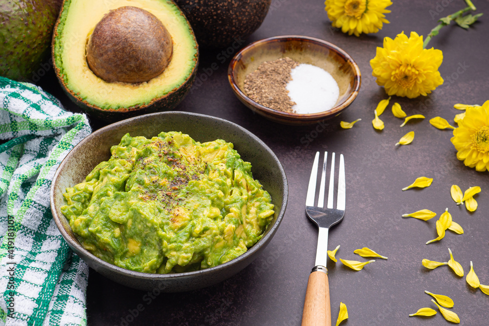 Fresh guacamole on a dish placed on a dark stone background with ingredients for homemade guacamole: avocados, lemon, salt, and pepper. Top view. Concept of traditional Mexican preparation Fresh guacamole on a dish placed on a dark stone background with ingredients for homemade guacamole: avocados, lemon, salt, and pepper. Top view. Concept of traditional Mexican preparation